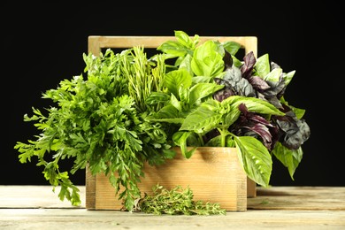 Photo of Different aromatic herbs in crate on wooden table against black background