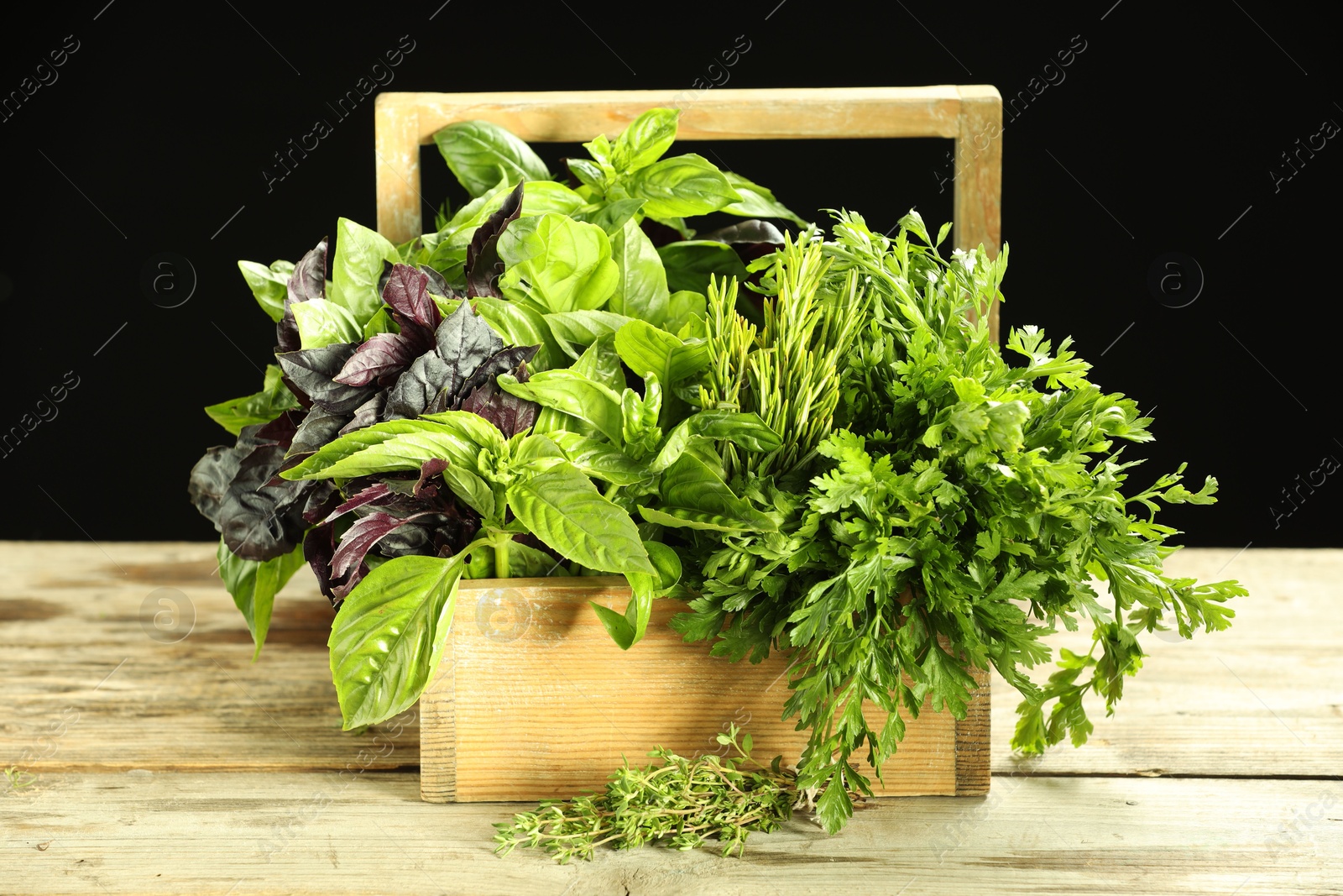 Photo of Different aromatic herbs in crate on wooden table against black background