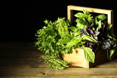 Photo of Different aromatic herbs in crate on wooden table against black background, space for text