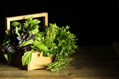 Photo of Different aromatic herbs in crate on wooden table against black background, space for text