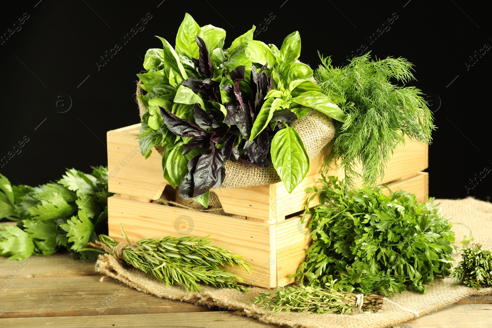 Photo of Different aromatic herbs in crate on wooden table against black background