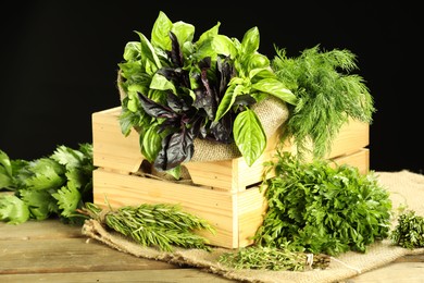 Photo of Different aromatic herbs in crate on wooden table against black background