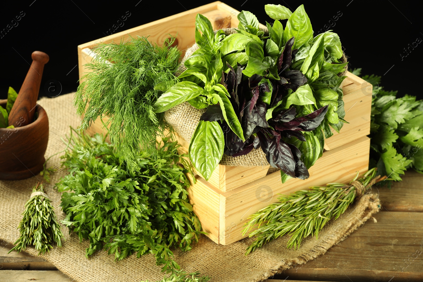 Photo of Different aromatic herbs in crate on wooden table against black background, closeup