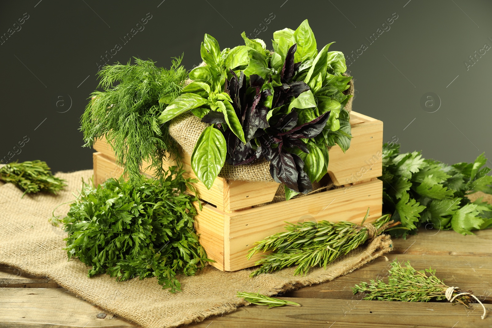 Photo of Different aromatic herbs in crate on wooden table against gray background