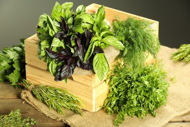 Photo of Different aromatic herbs in crate on wooden table against gray background, closeup