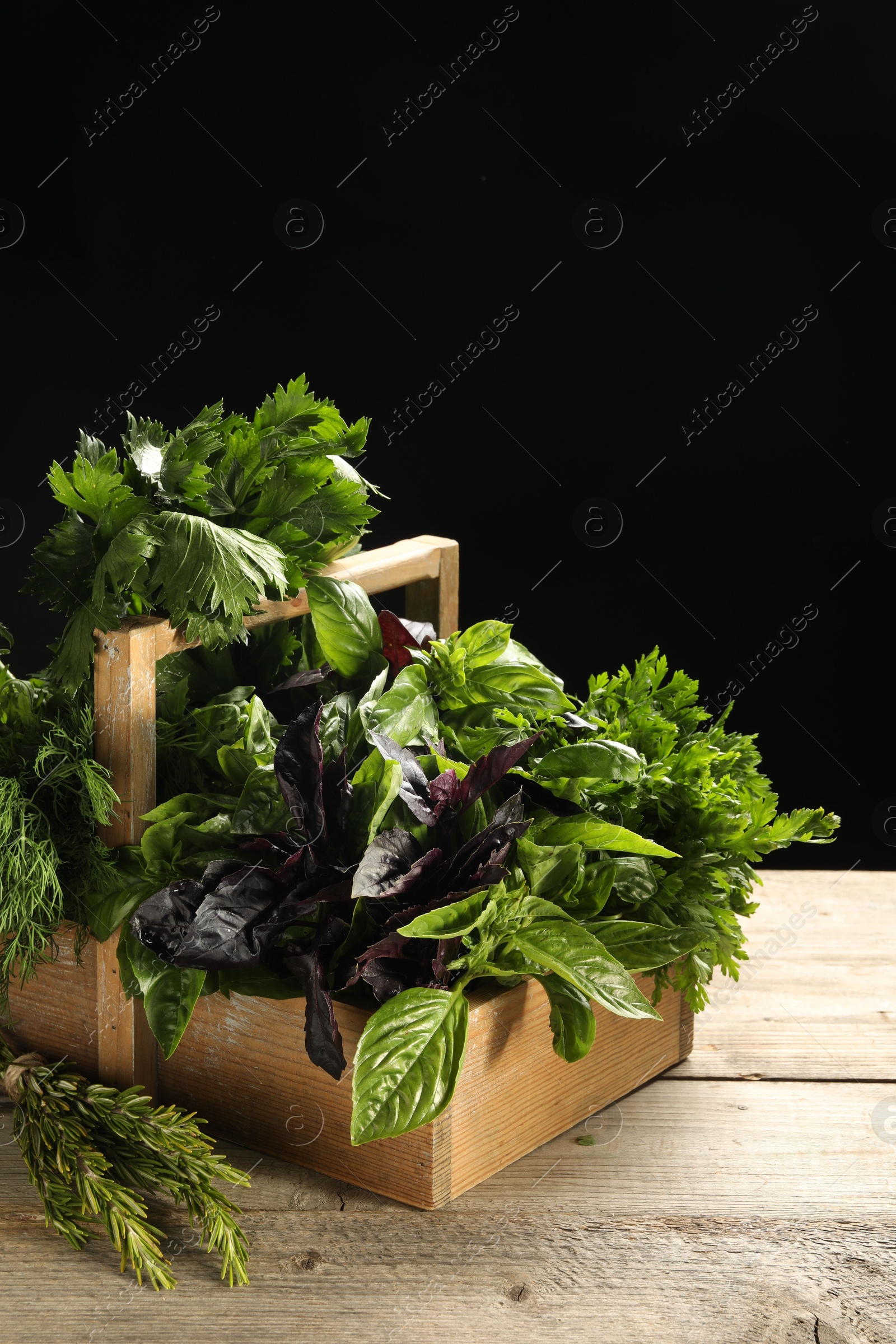 Photo of Different aromatic herbs in crate on wooden table against black background