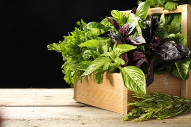 Photo of Different aromatic herbs in crate on wooden table against black background, space for text