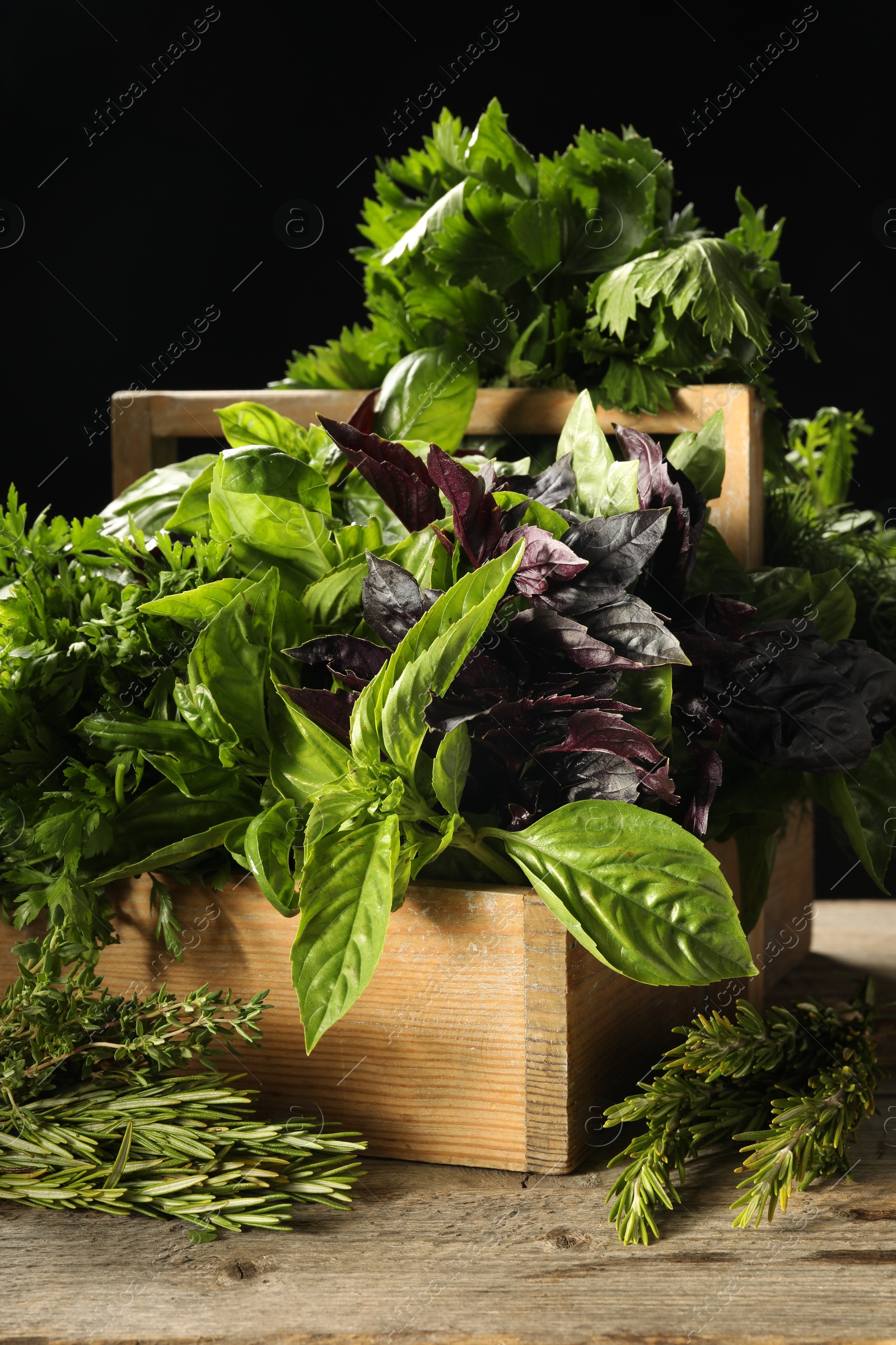 Photo of Different aromatic herbs in crate on wooden table against black background