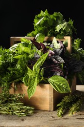 Different aromatic herbs in crate on wooden table against black background