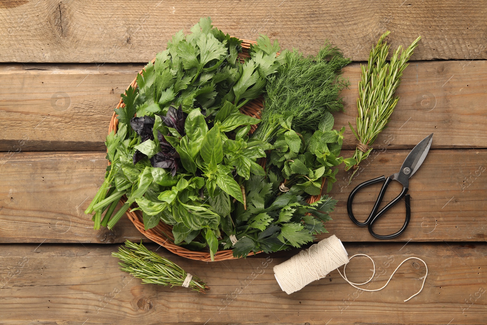 Photo of Different aromatic herbs in wicker basket, thread and scissors on wooden table, flat lay