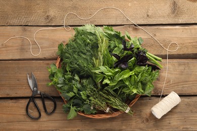 Photo of Different aromatic herbs in wicker basket, thread and scissors on wooden table, flat lay