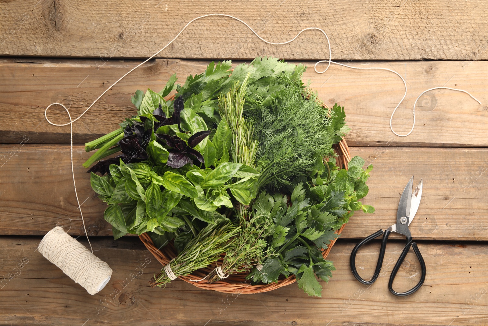 Photo of Different aromatic herbs in wicker basket, thread and scissors on wooden table, flat lay