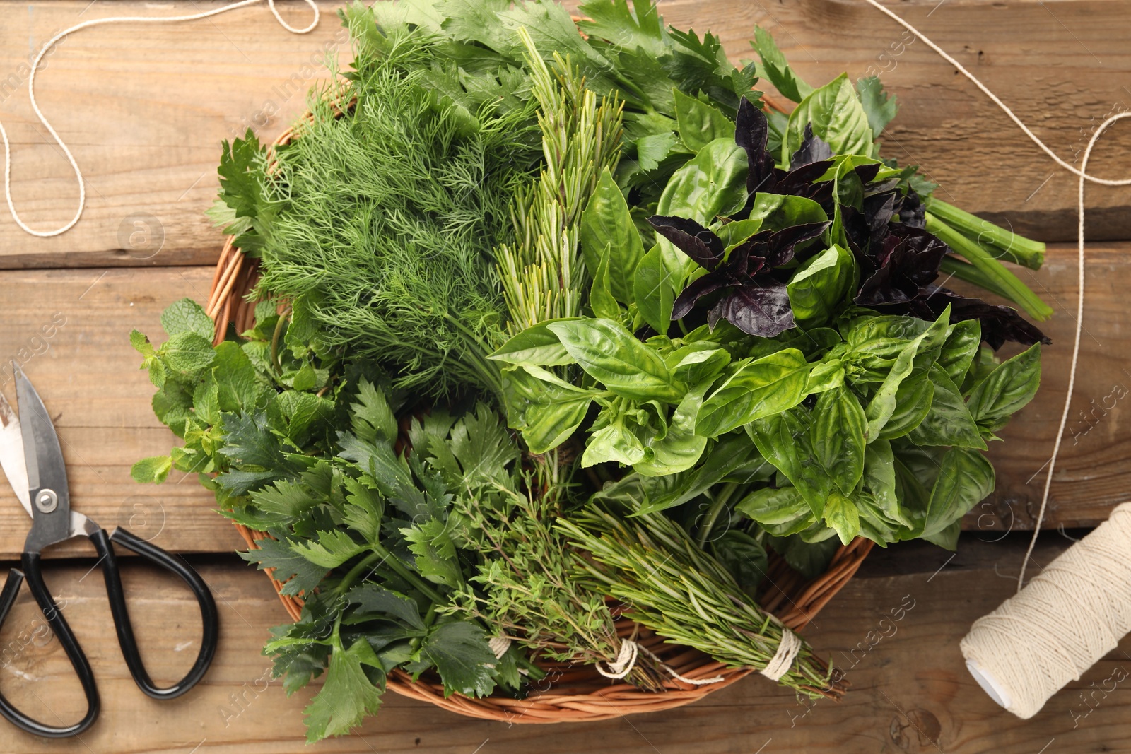 Photo of Different aromatic herbs in wicker basket, thread and scissors on wooden table, flat lay