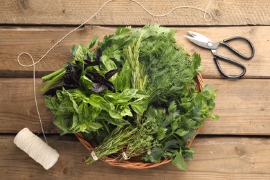 Photo of Different aromatic herbs in wicker basket, thread and scissors on wooden table, flat lay