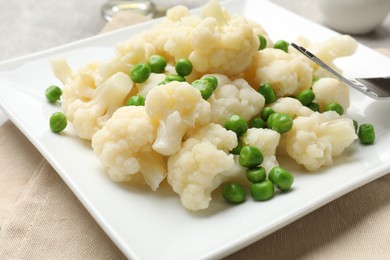 Photo of Tasty cooked cauliflower with green peas on table, closeup