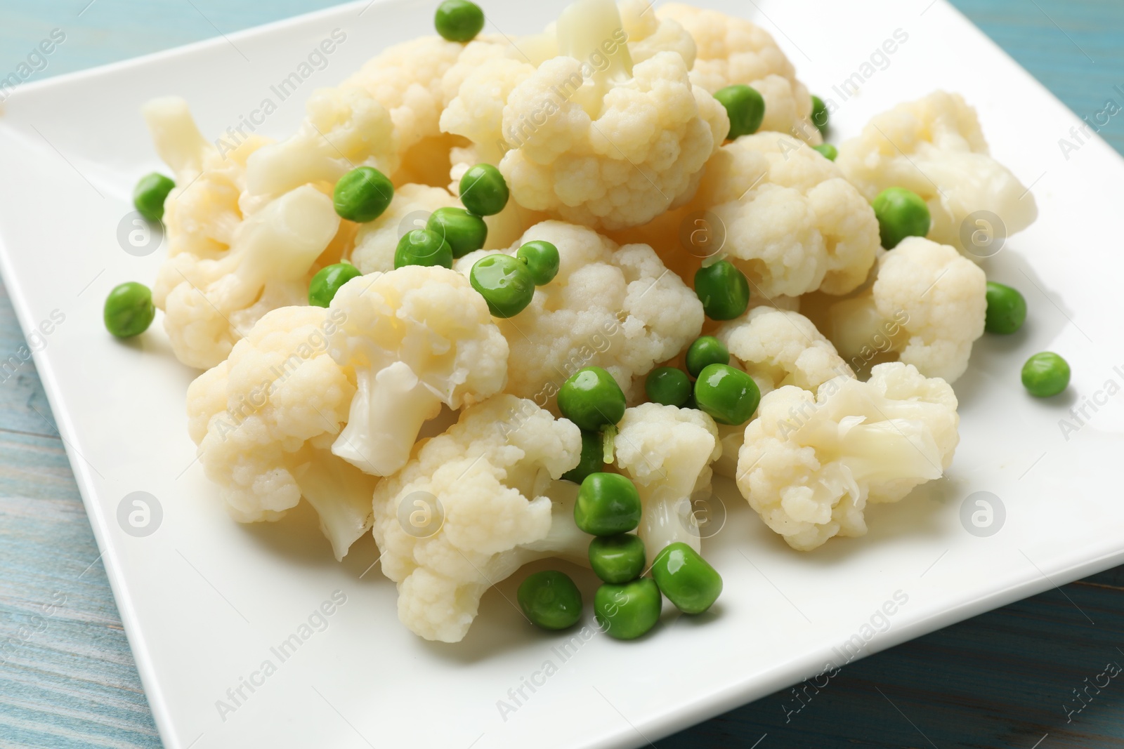 Photo of Tasty cooked cauliflower with green peas on light blue wooden table, closeup