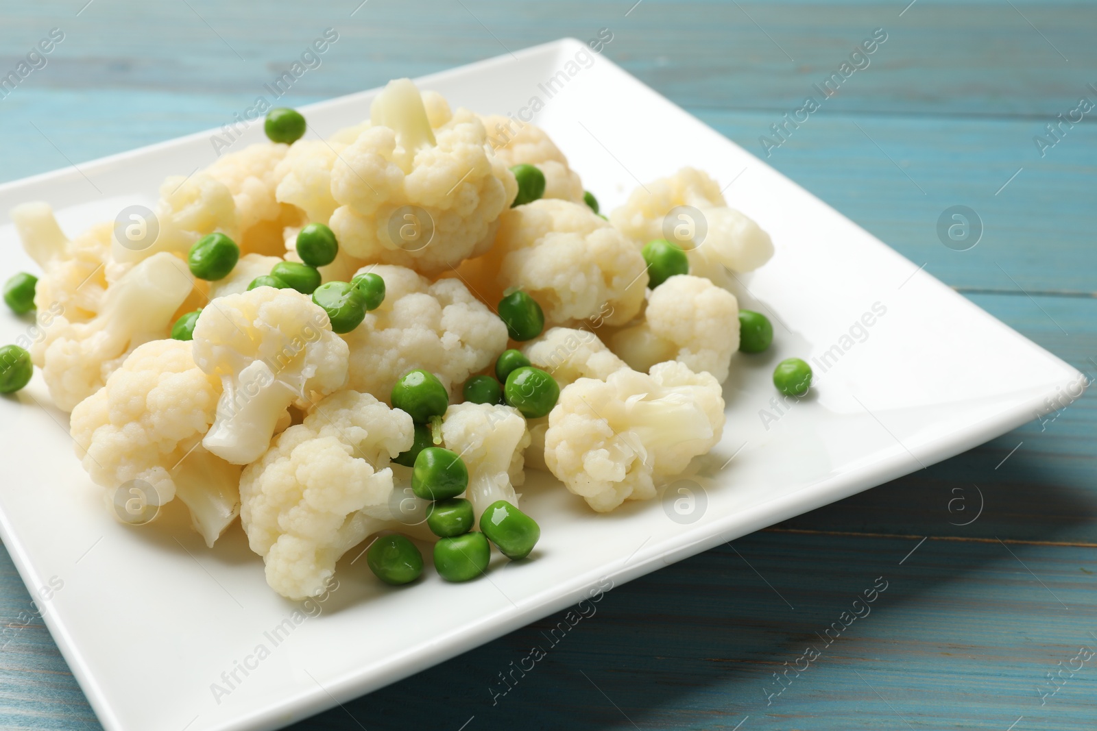 Photo of Tasty cooked cauliflower with green peas on light blue wooden table, closeup