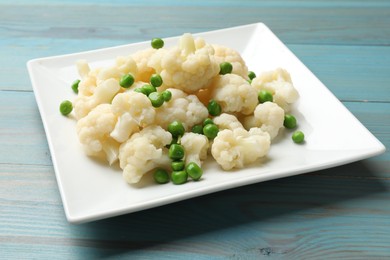 Photo of Tasty cooked cauliflower with green peas on light blue wooden table, closeup