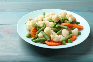 Photo of Tasty cooked cauliflower with green peas, string beans and carrot slices on light blue wooden table, closeup