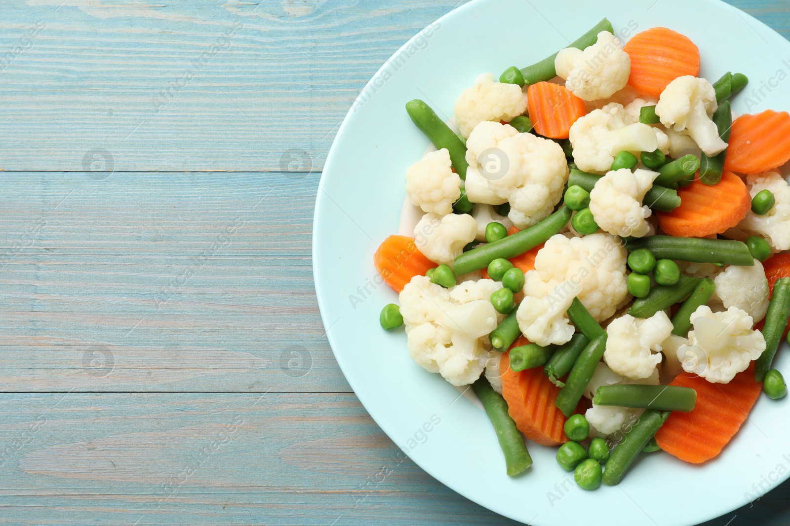 Photo of Tasty cooked cauliflower with green peas, string beans and carrot slices on light blue wooden table, top view. Space for text