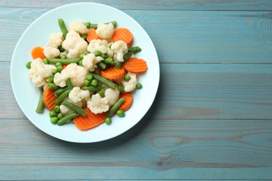 Photo of Tasty cooked cauliflower with green peas, string beans and carrot slices on light blue wooden table, top view. Space for text