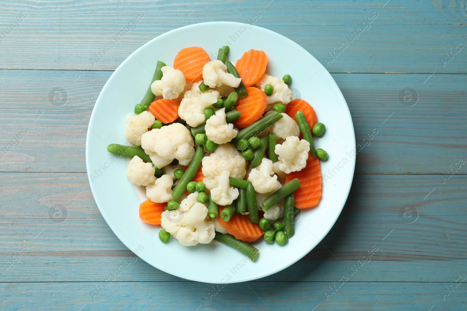 Photo of Tasty cooked cauliflower with green peas, string beans and carrot slices on light blue wooden table, top view