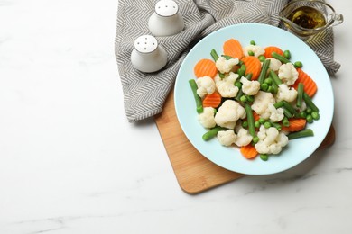 Photo of Tasty cooked cauliflower with green peas, string beans and carrot slices served on white marble table, flat lay. Space for text