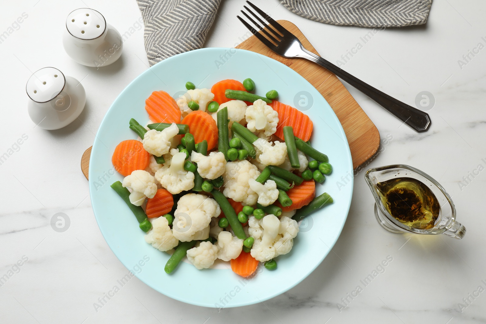 Photo of Tasty cooked cauliflower with green peas, string beans and carrot slices served on white marble table, flat lay