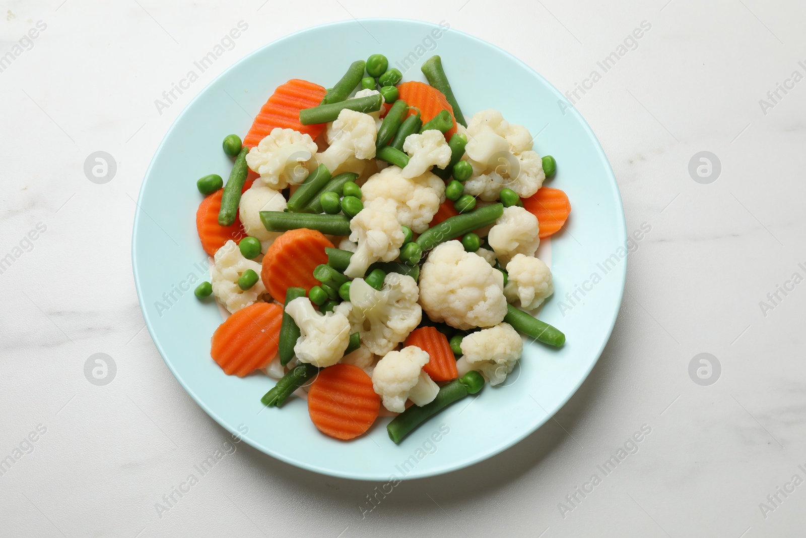 Photo of Tasty cooked cauliflower with green peas, string beans and carrot slices on white marble table, top view