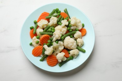 Photo of Tasty cooked cauliflower with green peas, string beans and carrot slices on white marble table, top view