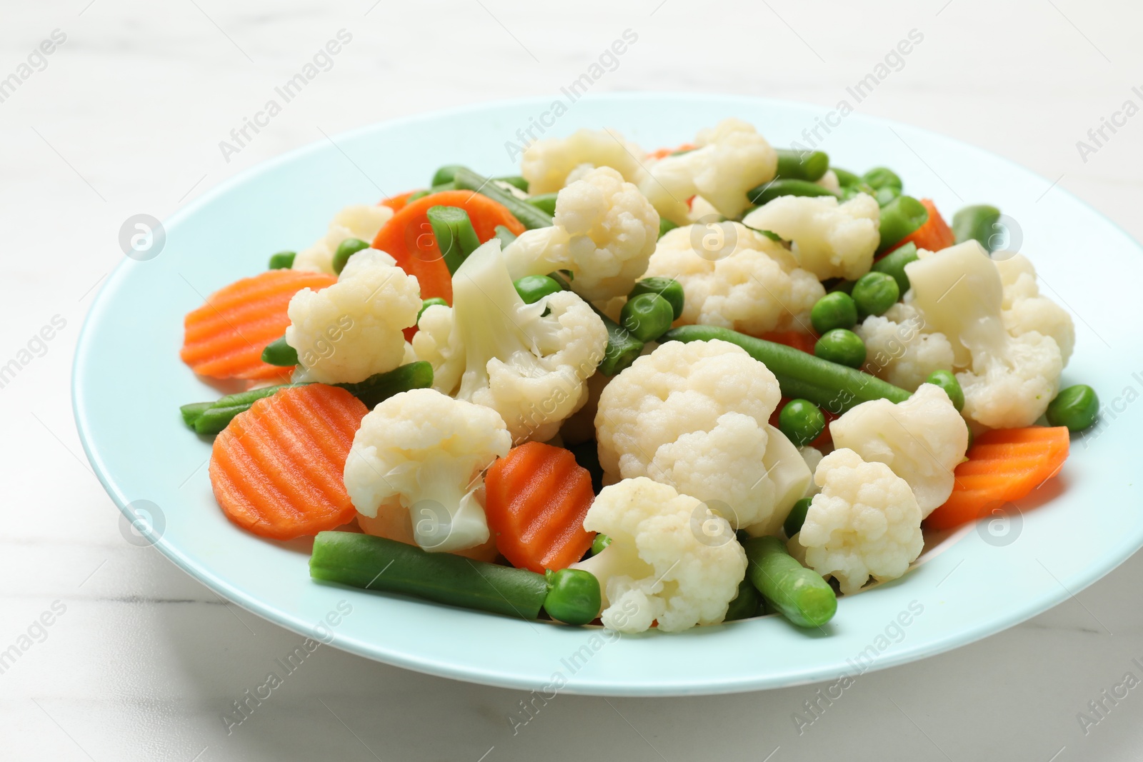 Photo of Tasty cooked cauliflower with green peas, string beans and carrot slices on white marble table, closeup