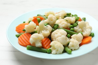 Photo of Tasty cooked cauliflower with green peas, string beans and carrot slices on white marble table, closeup