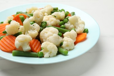 Photo of Tasty cooked cauliflower with green peas, string beans and carrot slices on white marble table, closeup