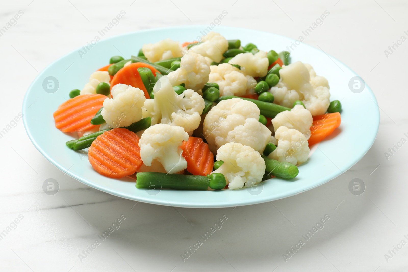 Photo of Tasty cooked cauliflower with green peas, string beans and carrot slices on white marble table, closeup