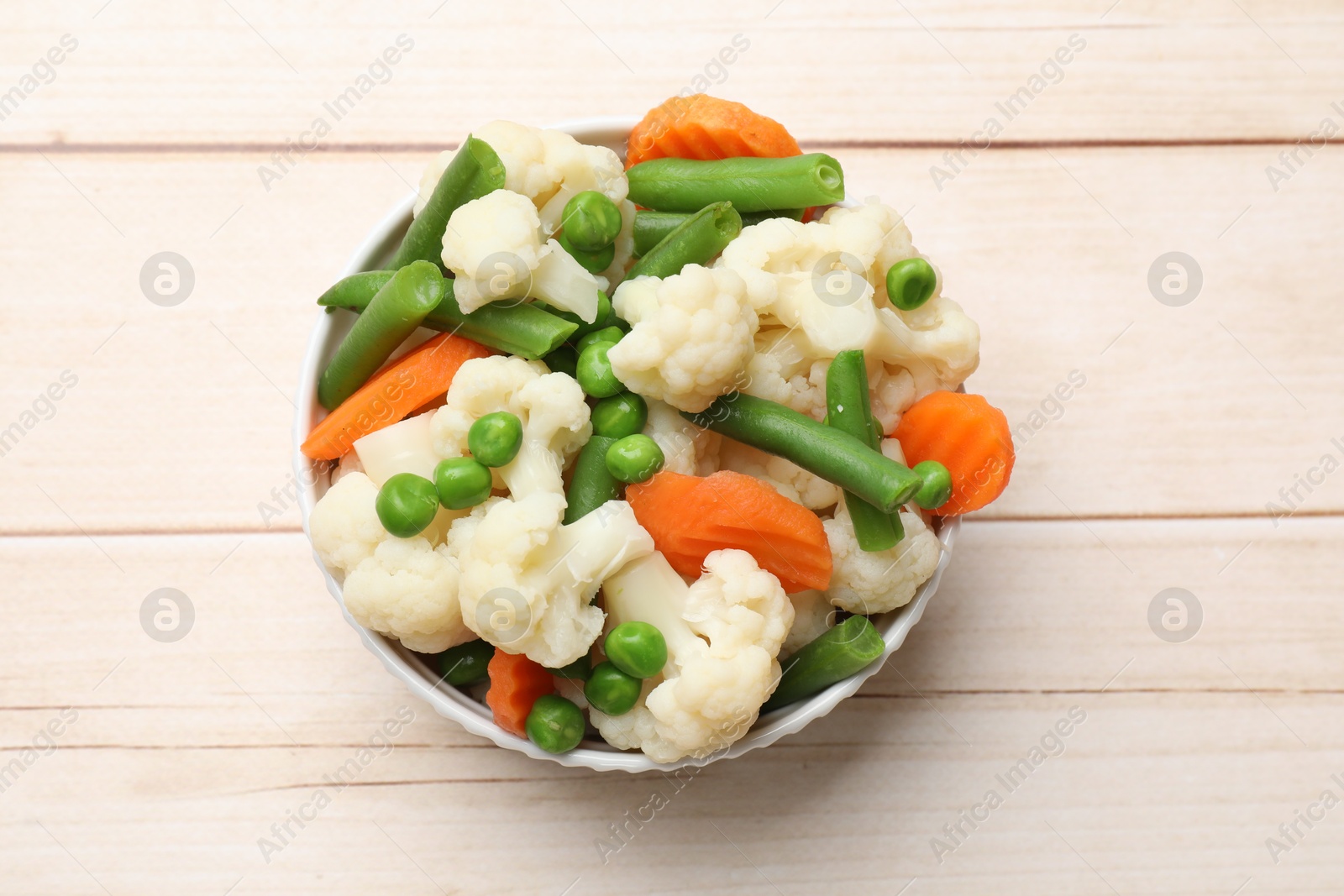 Photo of Tasty cooked cauliflower with green peas, string beans and carrot slices on white wooden table, top view