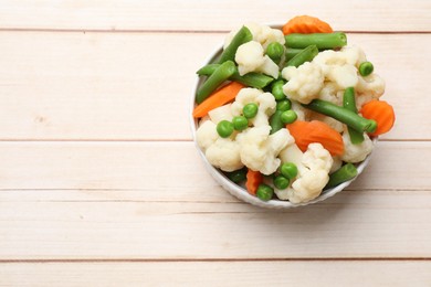 Photo of Tasty cooked cauliflower with green peas, string beans and carrot slices on white wooden table, top view. Space for text