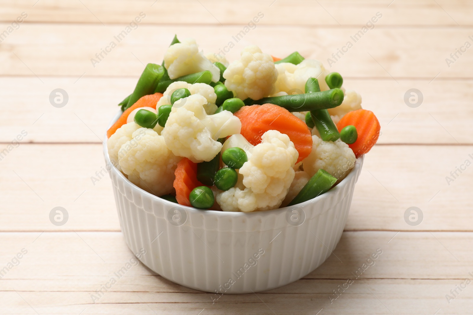 Photo of Tasty cooked cauliflower with green peas, string beans and carrot slices on white wooden table, closeup