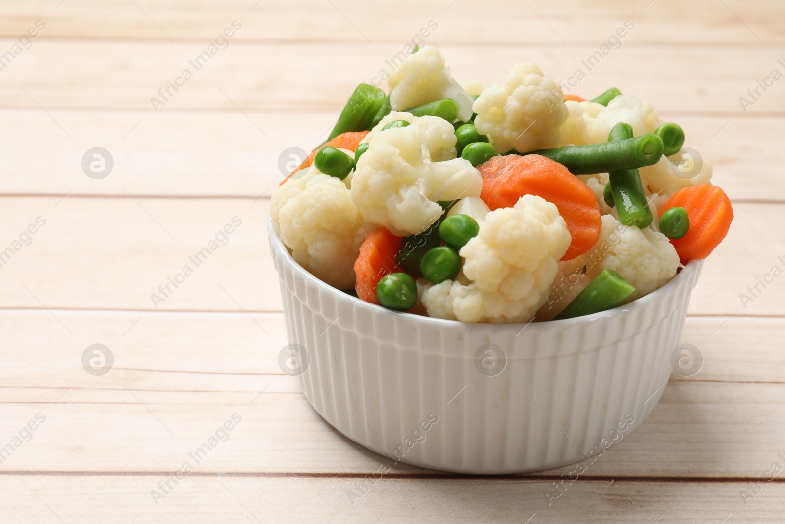 Photo of Tasty cooked cauliflower with green peas, string beans and carrot slices on white wooden table, closeup. Space for text