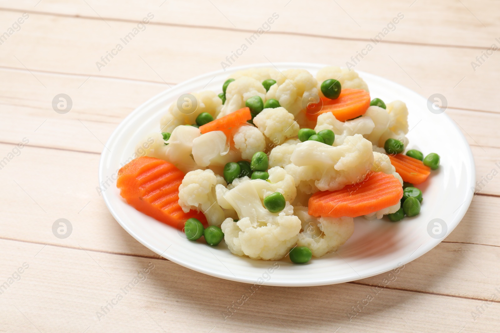 Photo of Tasty cooked cauliflower with green peas and carrot slices on white wooden table, closeup