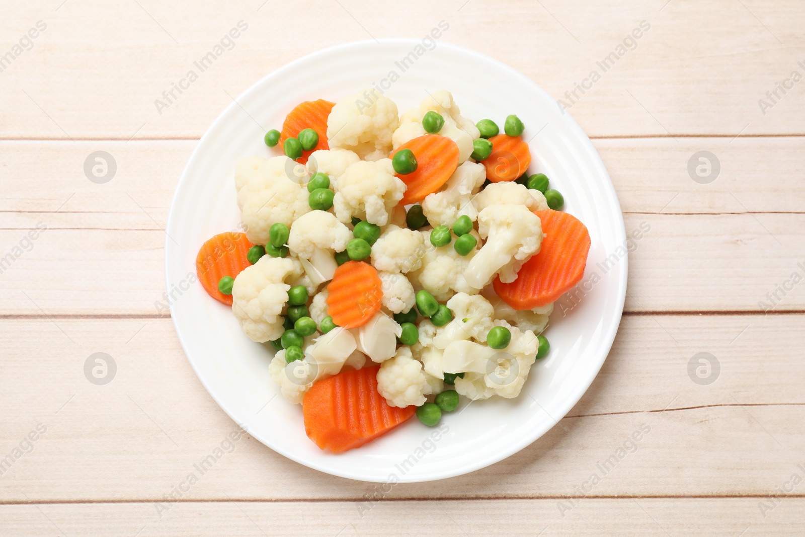 Photo of Tasty cooked cauliflower with green peas and carrot slices on white wooden table, top view