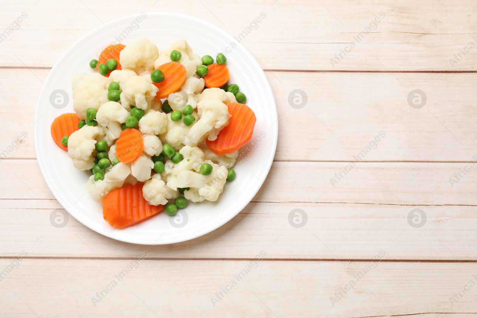 Photo of Tasty cooked cauliflower with green peas and carrot slices on white wooden table, top view. Space for text