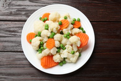 Photo of Tasty cooked cauliflower with green peas and carrot slices on wooden table, top view