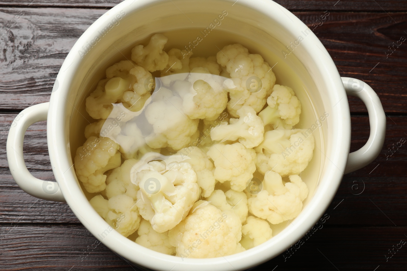 Photo of Cauliflower in pot with water on wooden table, above view