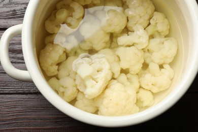 Photo of Cauliflower in pot with water on wooden table, closeup