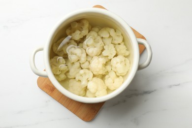 Photo of Cauliflower in pot with water on white marble table, top view