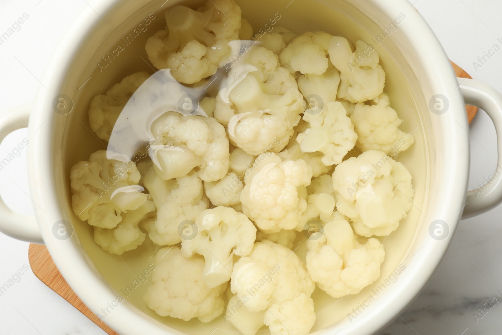 Photo of Cauliflower in pot with water on white marble table, top view