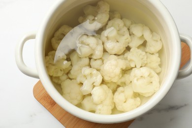 Photo of Cauliflower in pot with water on white marble table, above view