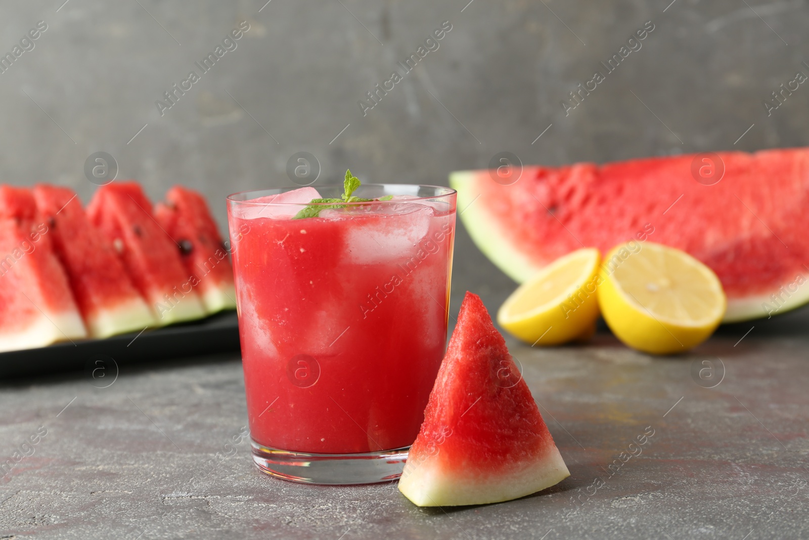 Photo of Tasty watermelon drink in glass, fresh fruits and mint on grey table