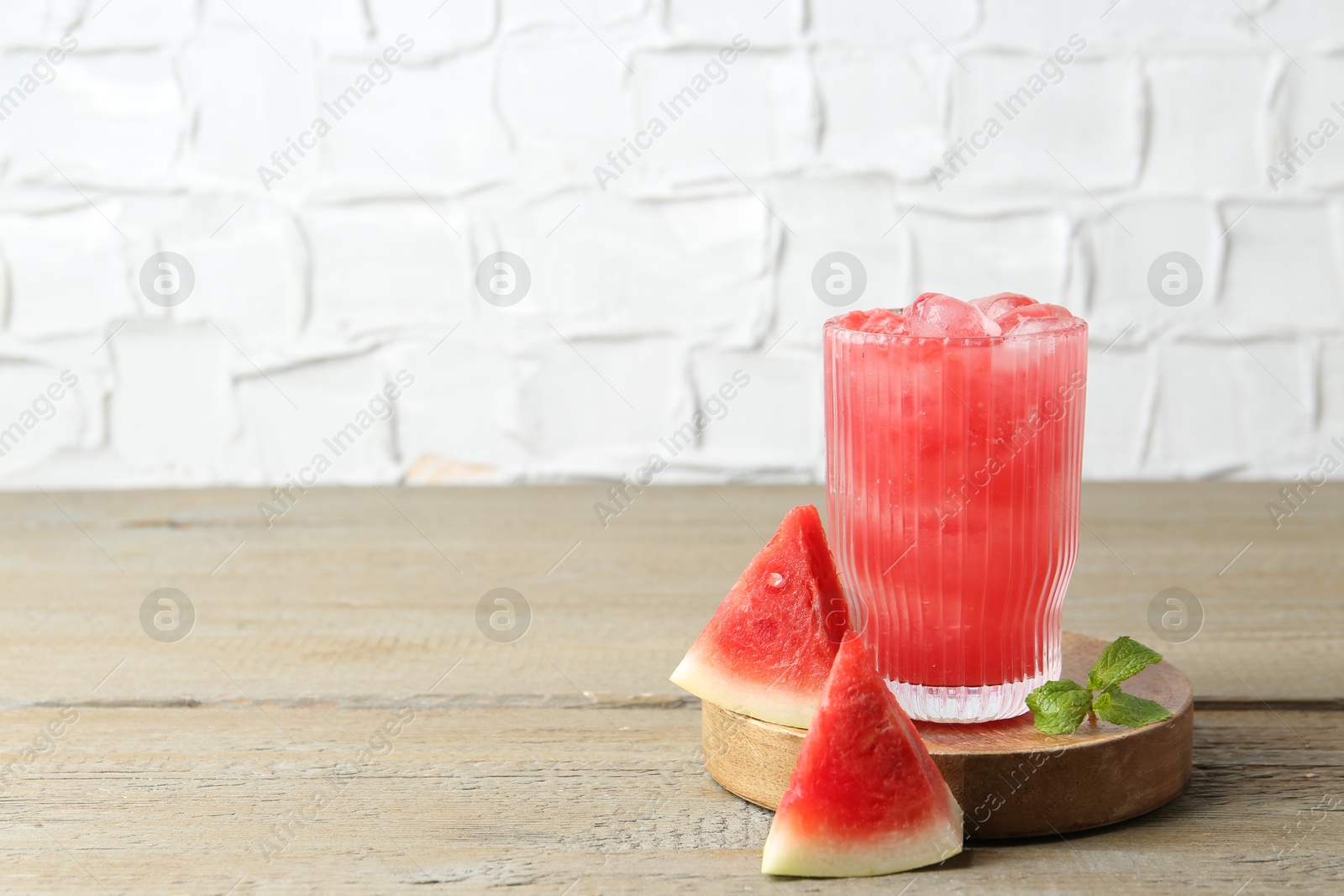 Photo of Tasty watermelon drink in glass, mint and fresh fruit on wooden table, space for text