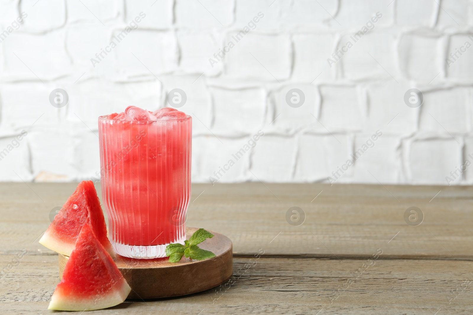 Photo of Tasty watermelon drink in glass, mint and fresh fruit on wooden table, space for text